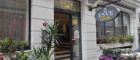 The exterior of the Esve Hotel with a visible entrance, steps leading up to the door, and potted plants outside.