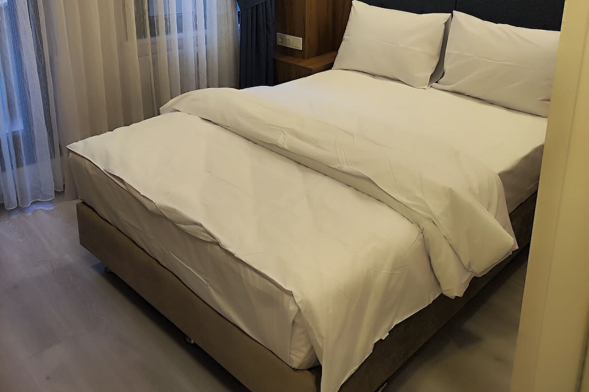 A hotel room with a large bed, a wooden headboard, and a bedside table with a lamp.