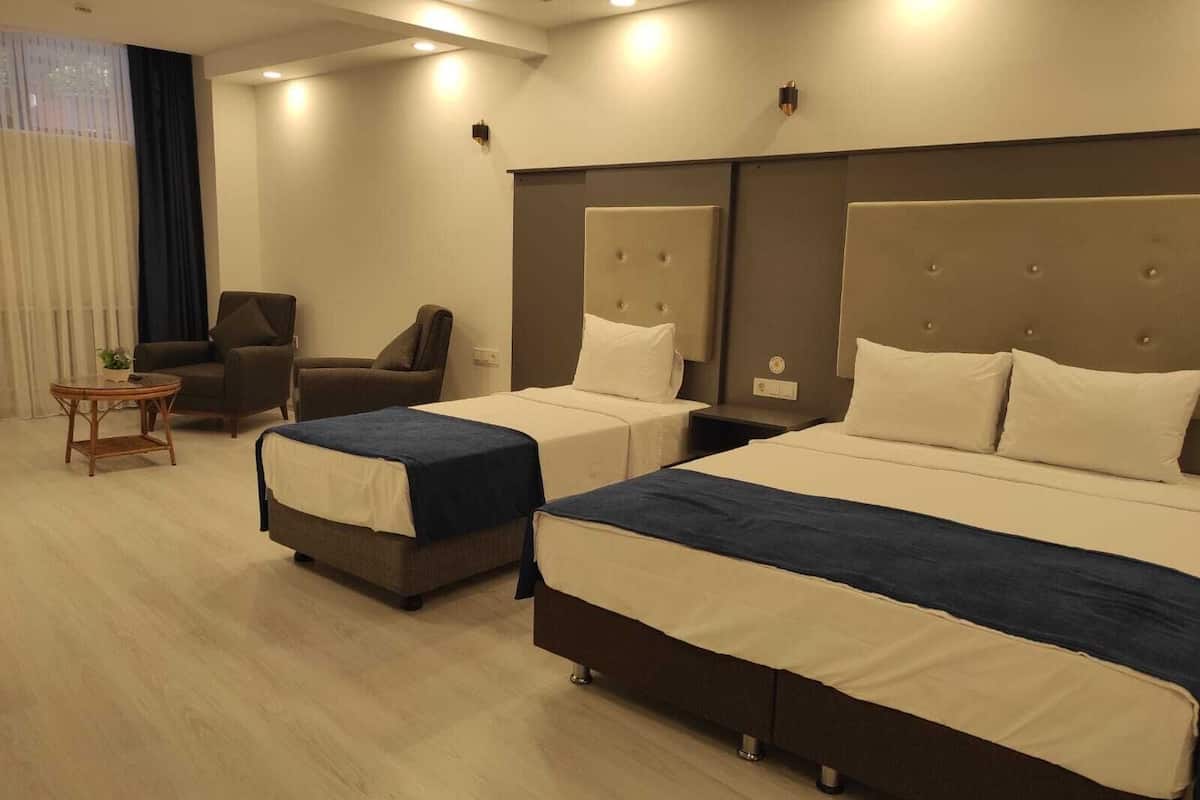 A hotel room with two beds, a chair, a small table, and a window with curtains.