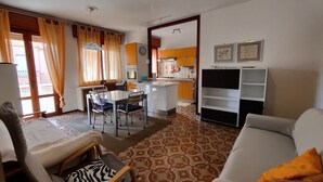 A living room with a sofa, a zebra-patterned chair, a dining table with chairs, and a kitchen area with orange cabinets. - Lively and Bright Flat in Caorle (Caorle)