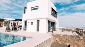 A modern white building with a swimming pool, outdoor seating, and a stone wall. - Casa Belvedere - Villa with fantastic views, completion January 2024! (Villaverde)