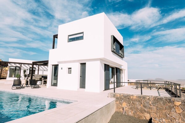 Un bâtiment moderne de couleur blanche, doté d’une piscine, d’un espace extérieur aménagé et d’un mur en pierre.