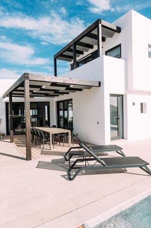 Une terrasse extérieure moderne, dotée d’une pergola en bois, d’une piscine et d’un espace repas avec des chaises et une table.