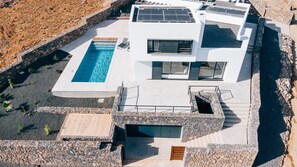 Une maison moderne dotée d’une piscine, de panneaux solaires et d’un chemin en pierre.