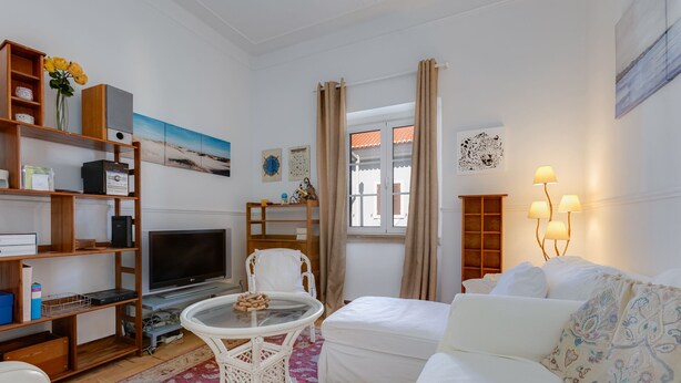 A well-lit living room with a flat-screen TV, white furniture, a bookshelf, and a window with curtains. - Charming house for 6 persons at downtown Faro (Faro)