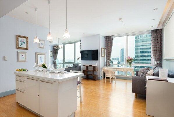 A modern living room with a central island, a flat-screen TV, and a city view through large windows.