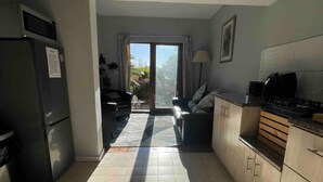 Eine geräumige Küche mit Kühlschrank, Herd und Schränken. Es gibt einen Essbereich mit Tisch und Stühlen, sowie einen Blick ins Freie durch eine Glastür.