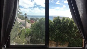 Ein Fenster mit Blick auf eine Küstenlandschaft, einschließlich eines Gebäudes und üppiger Vegetation.