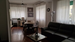 Un salon avec un canapé, une table à manger avec des chaises, un coin cuisine avec une cuisinière et une horloge au mur.
