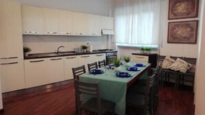 Une cuisine compacte avec des meubles blancs, une table à manger dressée avec de l’assiette bleue et un canapé agrémenté de coussins à rayures.