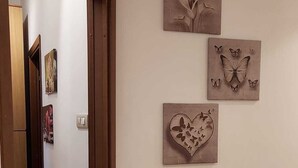 Un couloir doté d’un plancher en bois, une porte donnant sur une autre pièce, et trois œuvres d’art fixées au mur représentant des fleurs, des papillons et un cœur orné de papillons.