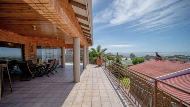 A covered outdoor area with a dining setup, a view of the landscape, and a red-roofed building in the background. - JBayholiday (Jeffreys Bay)