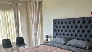 A bedroom with a large bed, two chairs, a nightstand, and a lamp. - JBayholiday (Jeffreys Bay)