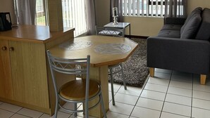 A compact living space with a kitchenette, a dining table with chairs, a sofa, and a window with curtains. - JBayholiday (Jeffreys Bay)