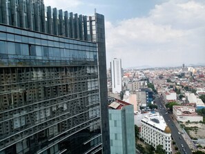 Um moderno edifício alto com fachada de vidro refletivo, uma torre branca imponente e vista para o horizonte urbano com vários edifícios e ruas.