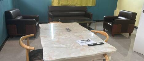 A meeting room with a marble table, four wooden chairs, a sofa, and a yellow curtain.