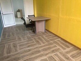 Um quarto pequeno com uma mesa, uma cadeira, uma porta e uma parede amarela.