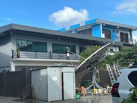 Um edifício moderno com uma antena parabólica, um pequeno galpão e um carro branco estacionado nas proximidades.