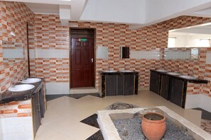 A bathroom with patterned walls, multiple sinks, a wooden door, and a tiled floor. - Greenyard Resort Mtwapa (Mtwapa)