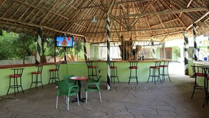 A covered outdoor seating area with tables and chairs, a TV screen, and a thatched roof. - Greenyard Resort Mtwapa (Mtwapa)