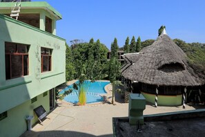 A pool area with a thatched-roof hut, a green building, and a clear blue sky. - Greenyard Resort Mtwapa (Mtwapa)