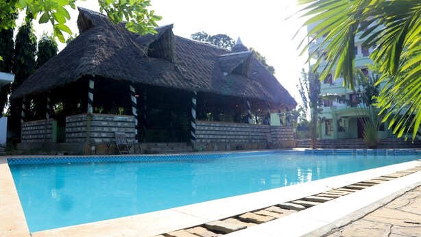 A swimming pool with a thatched-roof structure adjacent to it. - Greenyard Resort Mtwapa (Mtwapa)