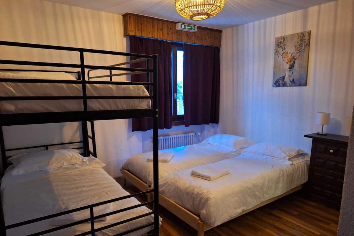 A room with bunk beds, a wooden dresser, a painting, and a window with curtains.