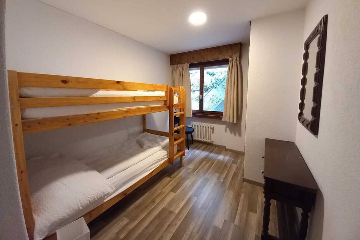 A bunk bed room with a wooden desk and a window with curtains.