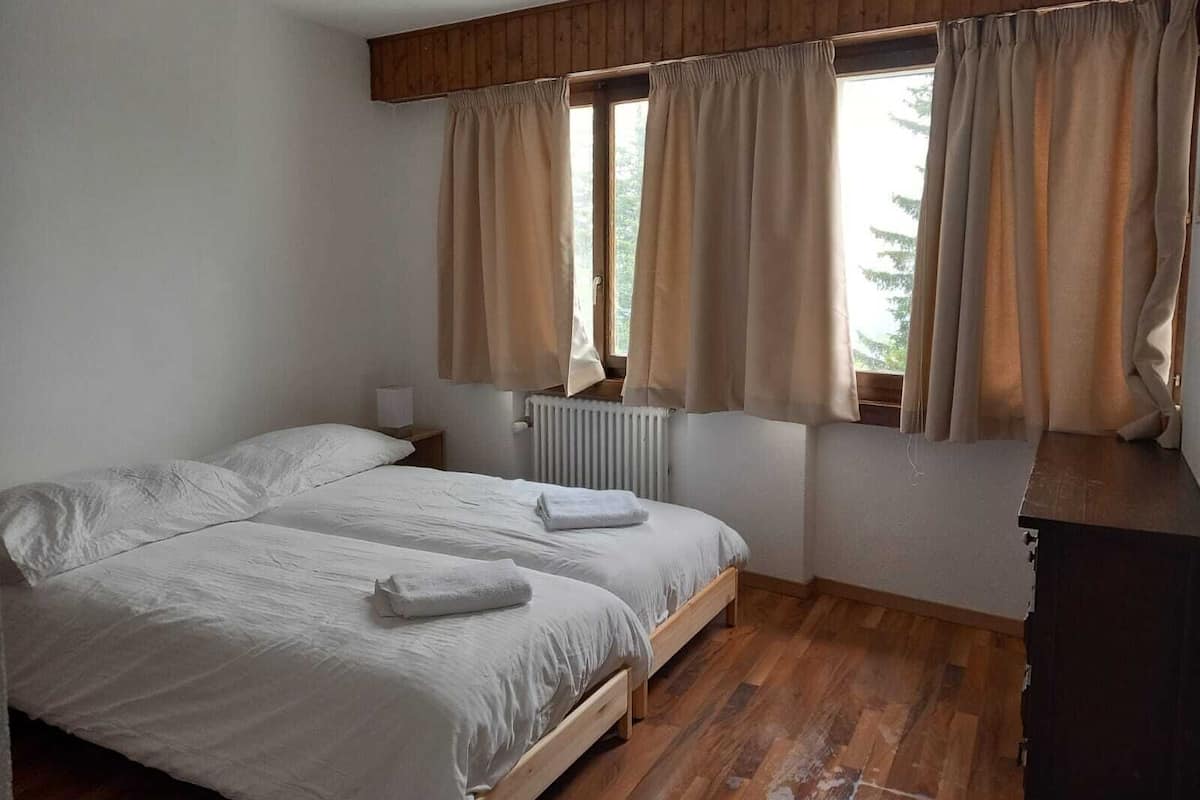 A bedroom with two beds, wooden flooring, a window with curtains, and a radiator.