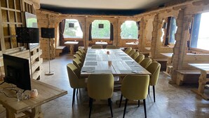 A large wooden dining area with a long table and chairs, surrounded by windows with views of greenery. - Auberge de l'Ours (Vex)