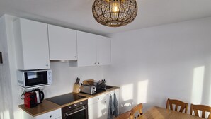 A compact kitchen with white cabinets, a microwave, a toaster, and a wooden dining table with chairs. - Auberge de l'Ours (Vex)