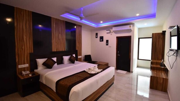 A modern hotel room with a large bed, wooden headboard, and a ceiling fan. - Hotel SRI KPN (Port Blair)