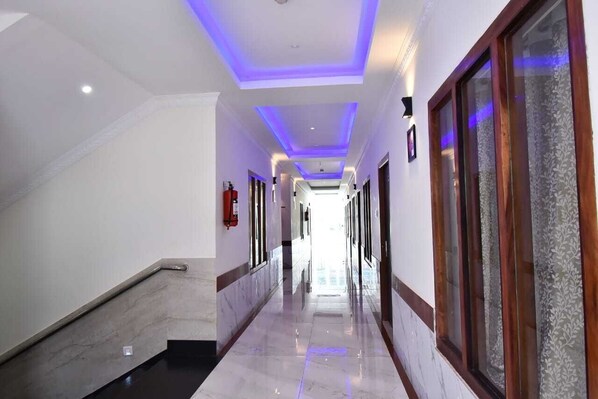 A hotel corridor with a marble floor, a staircase on the left, and a wooden-framed window on the right. - Hotel SRI KPN (Port Blair)