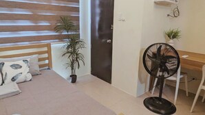 Ein Schlafzimmer mit Bett, Nachttisch, Schreibtisch mit Stuhl, Klimaanlage und einer Topfpflanze.