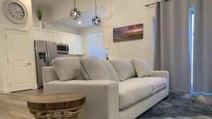 Una sala de estar moderna con un sofá, una mesita redonda de madera y una cocina al fondo.