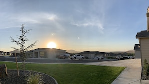 Una calle residencial con casas, cielo despejado y el sol poniéndose.