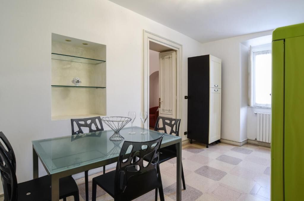 Un comedor pequeño con una mesa de vidrio y sillas negras, una puerta blanca y un armario verde.