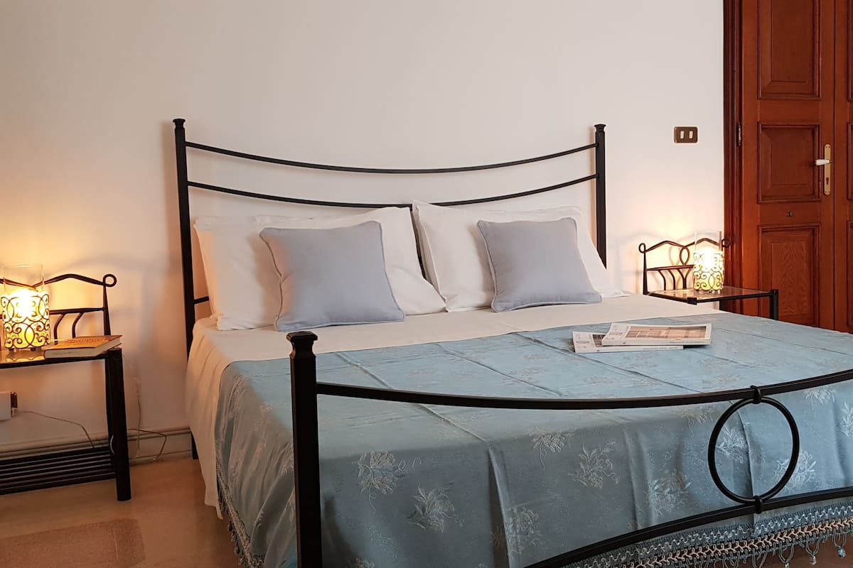 A neatly made bed with a blue bedspread and two pillows, flanked by bedside tables with lamps.