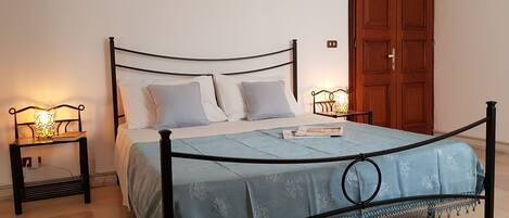A neatly made bed with a blue bedspread and two pillows, flanked by bedside tables with lamps.