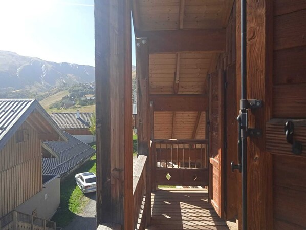 A wooden staircase leading to a balcony with a view of a village and mountains.