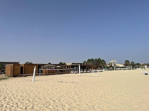 A beach with a volleyball net, wooden structures, and a clear sky.
