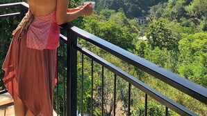 A person standing on a balcony overlooking a lush valley with mountains in the distance.