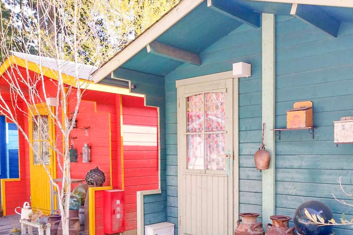 Une maison aux couleurs vives, avec une porte rouge, une façade bleue et un petit porche agrémenté d’une cage à oiseaux et d’une plante en pot.