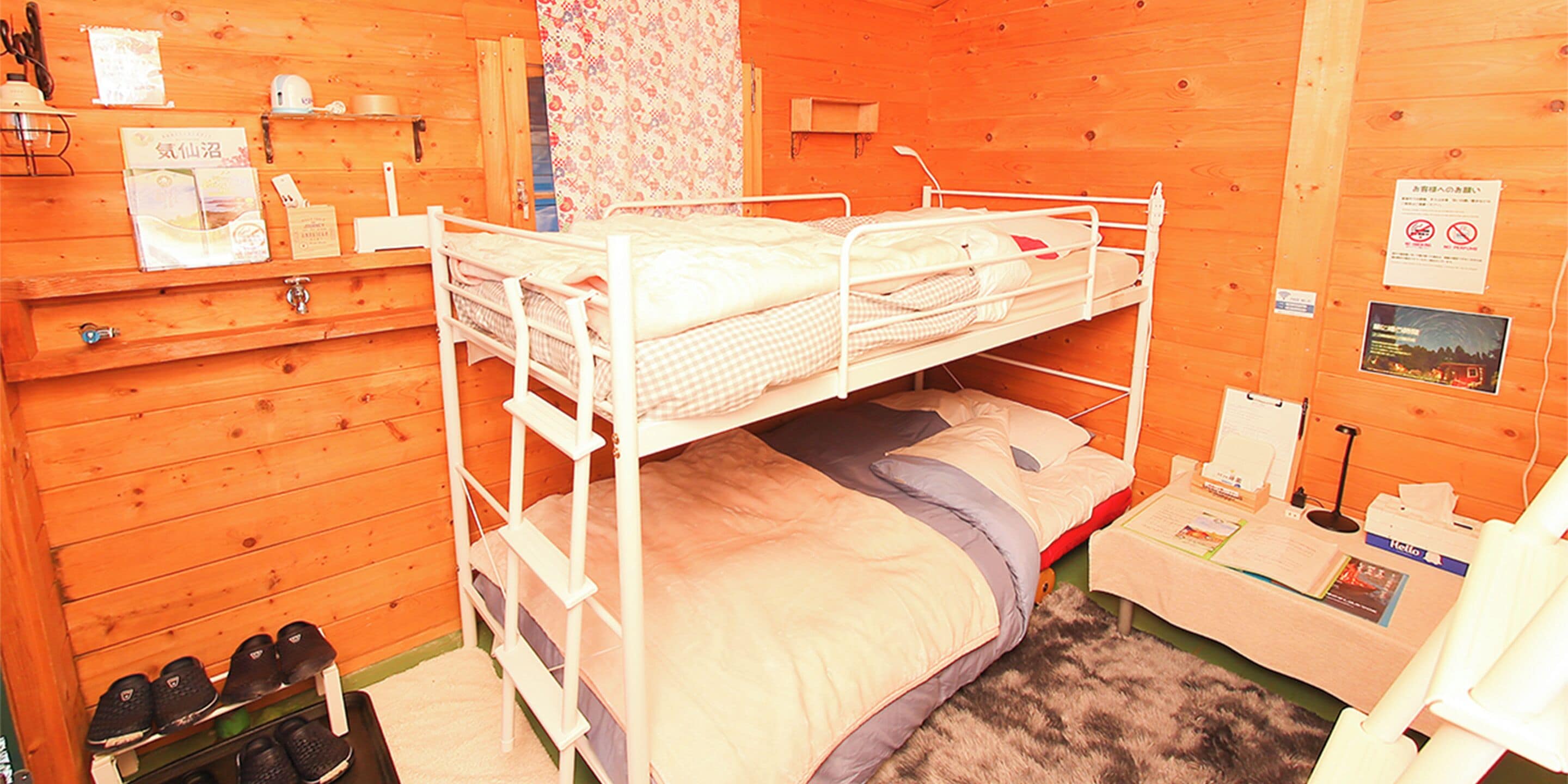Camere con letti a castello, pareti in legno, una piccola scrivania e un porta scarpe.