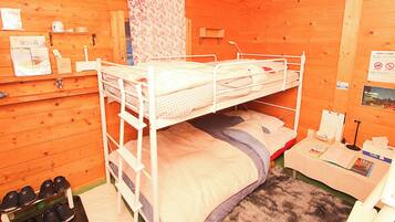 Camere con letti a castello, pareti in legno, una piccola scrivania e un porta scarpe.