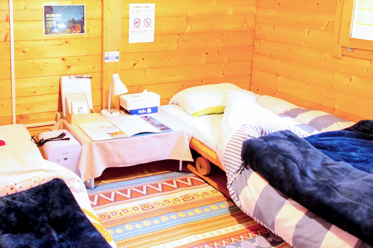 Una habitación pequeña y acogedora con dos camas individuales, una mesita de noche con lámpara, una pequeña mesa y un cuadro colgado en la pared.