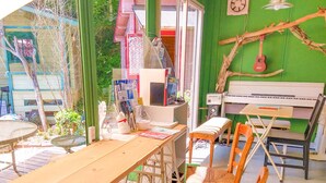 A room with a wooden table, a small white cabinet, a chair, a keyboard, and a window with a view of greenery. - Forest Cottage Kesennuma (Kesennuma)