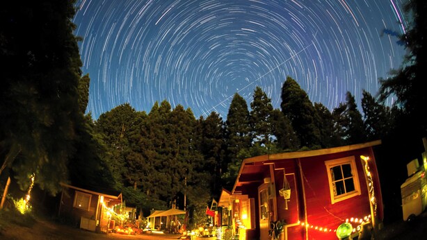 A night scene with a star trail effect in the sky, surrounded by a forest and illuminated buildings. - Forest Cottage Kesennuma (Kesennuma)