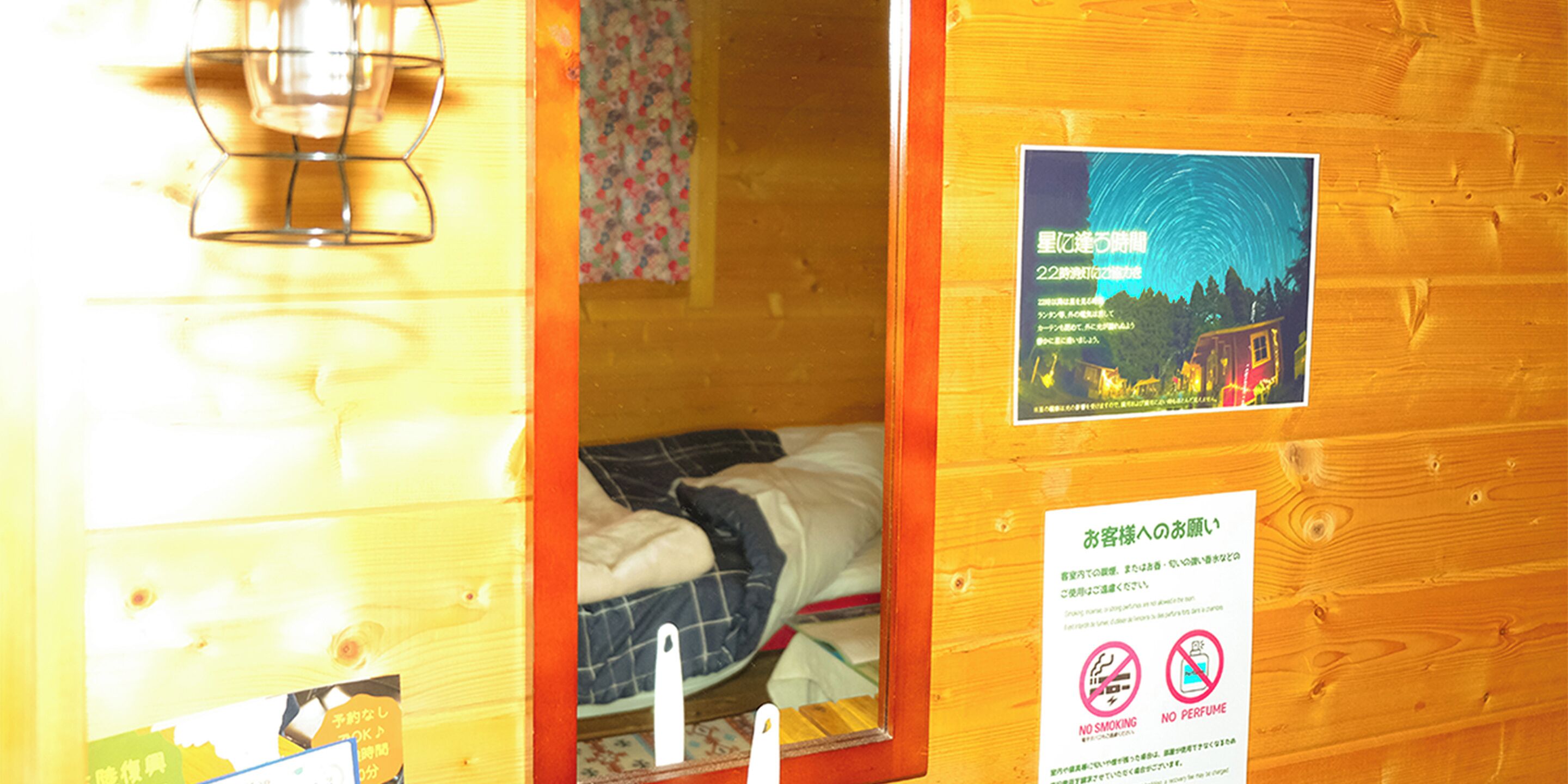 A wooden cabin interior with a bed, a hanging light fixture, and a poster on the wall.