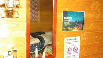 Interior de una cabaña de madera con una cama, una lámpara colgante y un cartel en la pared.